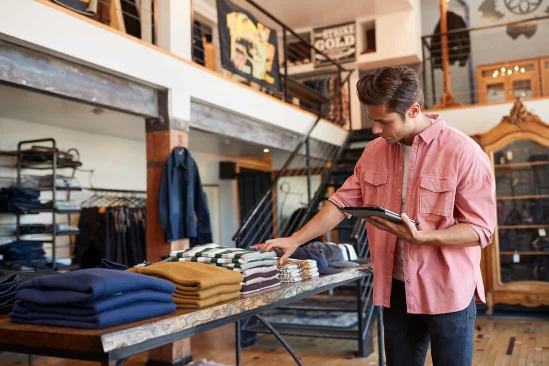 Male retail employee checks stock counts of shirts