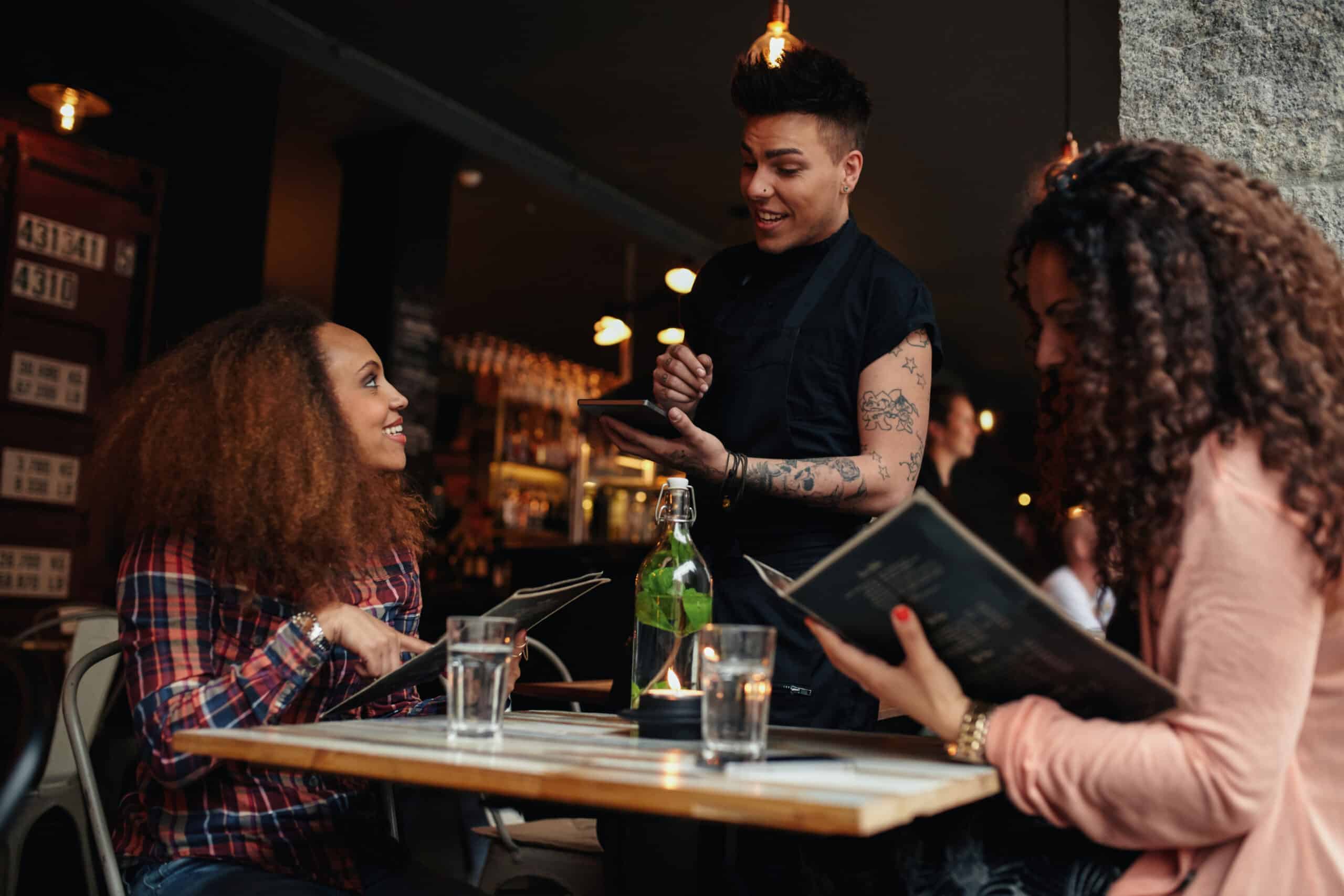 Young woman with a friend ordering to waiter holding digital tablet. 
